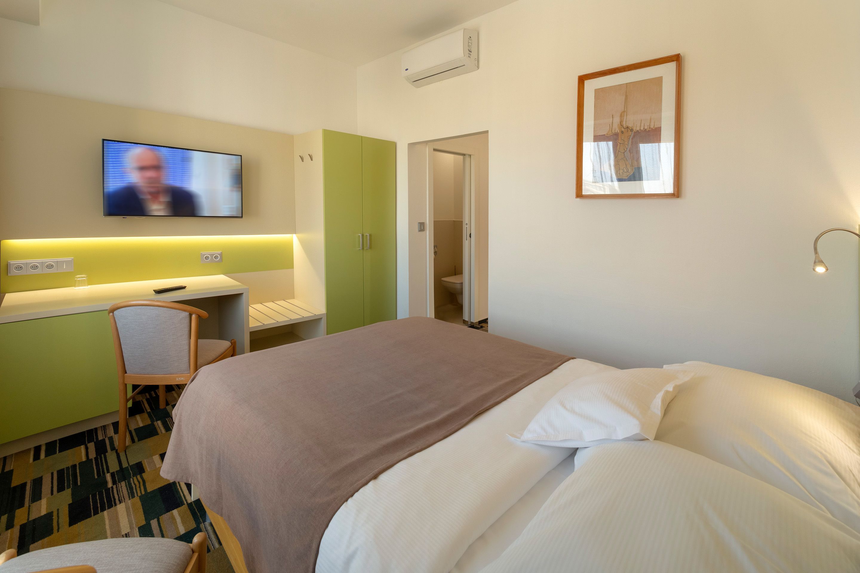 Ein Hotelzimmer mit einem Bett, einem Schreibtisch, einem Stuhl, einem Fernseher und einem gerahmten Bild an der Wand.