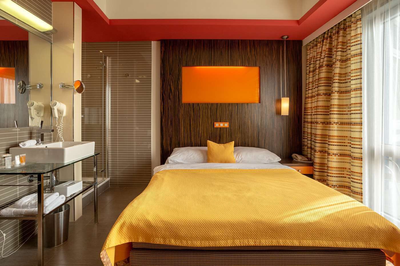 Hotellihuone, jossa on suuri sänky, lasinen yöpöytä, moderni kylpyhuone suihkulla sekä suuri ikkuna, jossa on verhot.