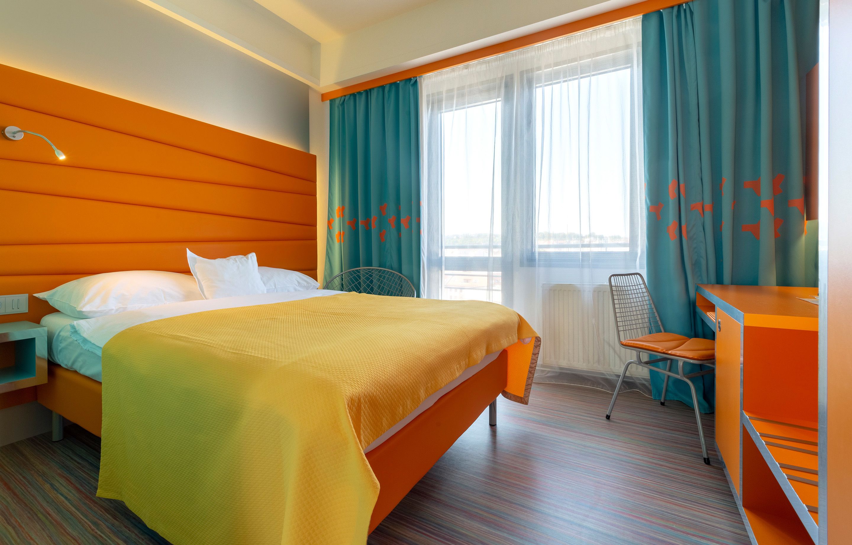 A hotel room with a bed, a desk, a chair, and a window with curtains.
