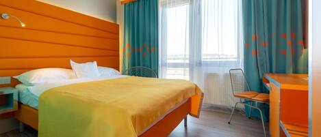 Una habitación de hotel con cama, escritorio, silla y ventana con cortinas.