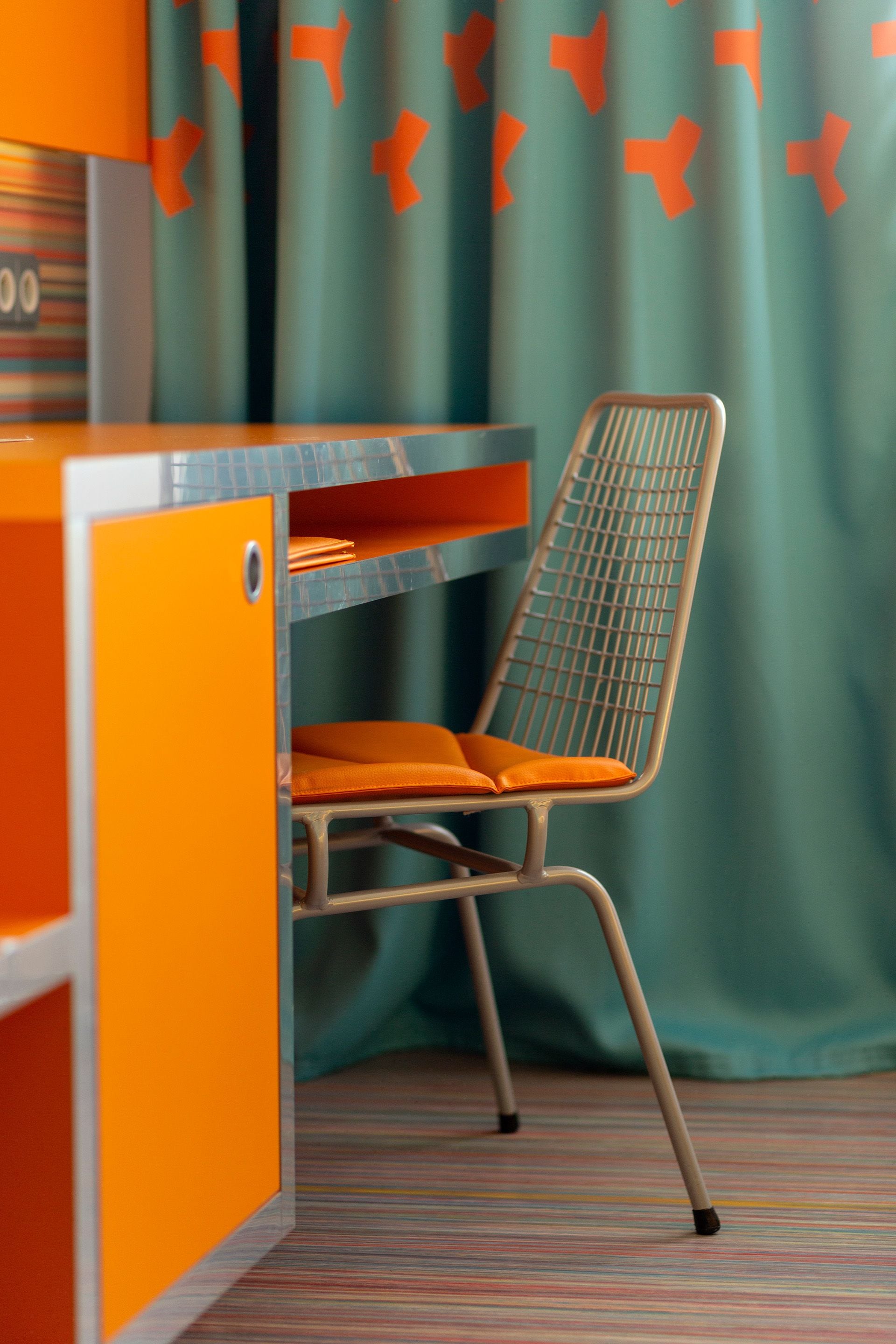 A compact, orange and teal-colored room with a metal-framed chair and a small desk.