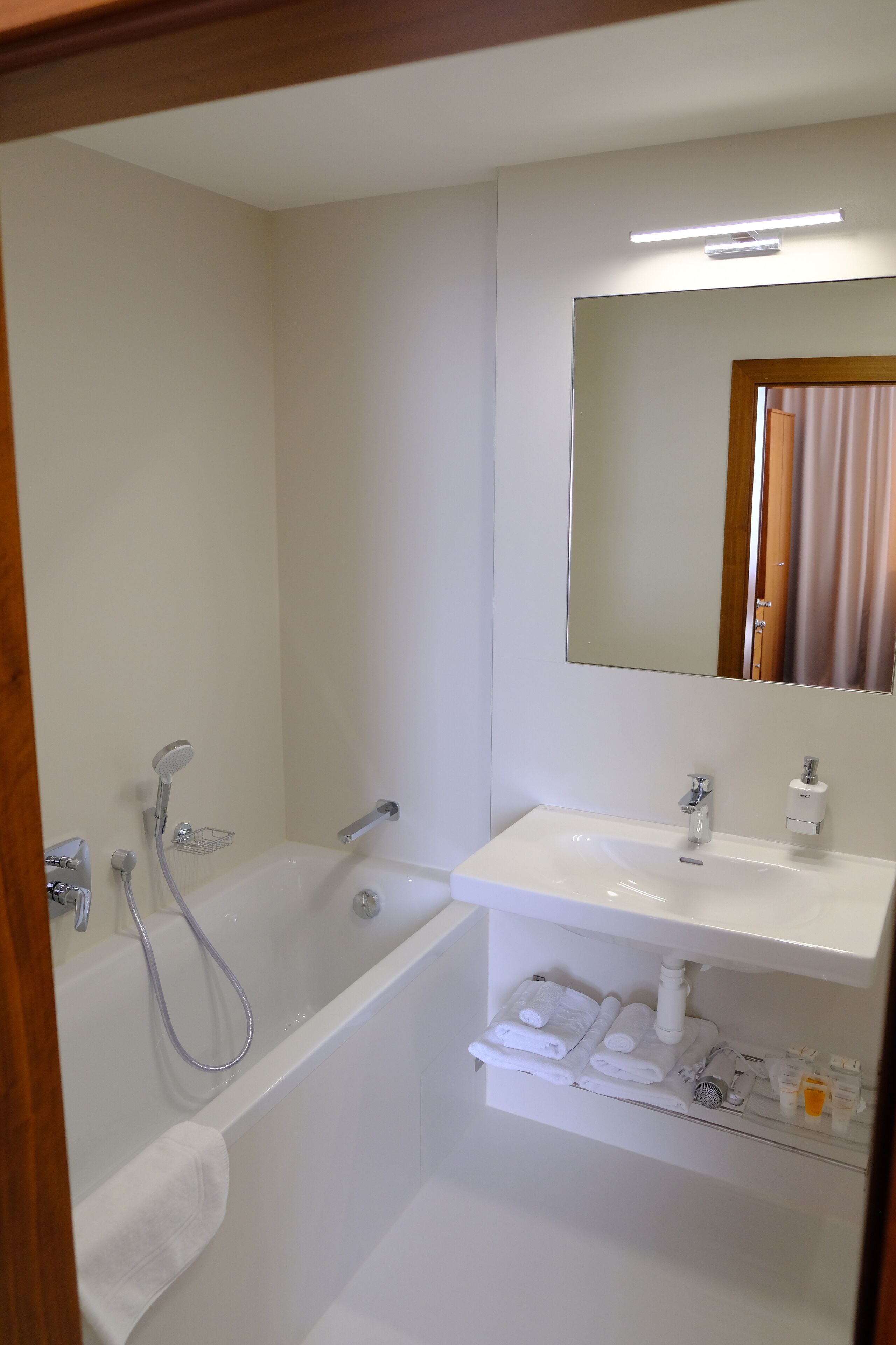 A bathroom with a bathtub, a sink, a mirror, and a shelf with toiletries.