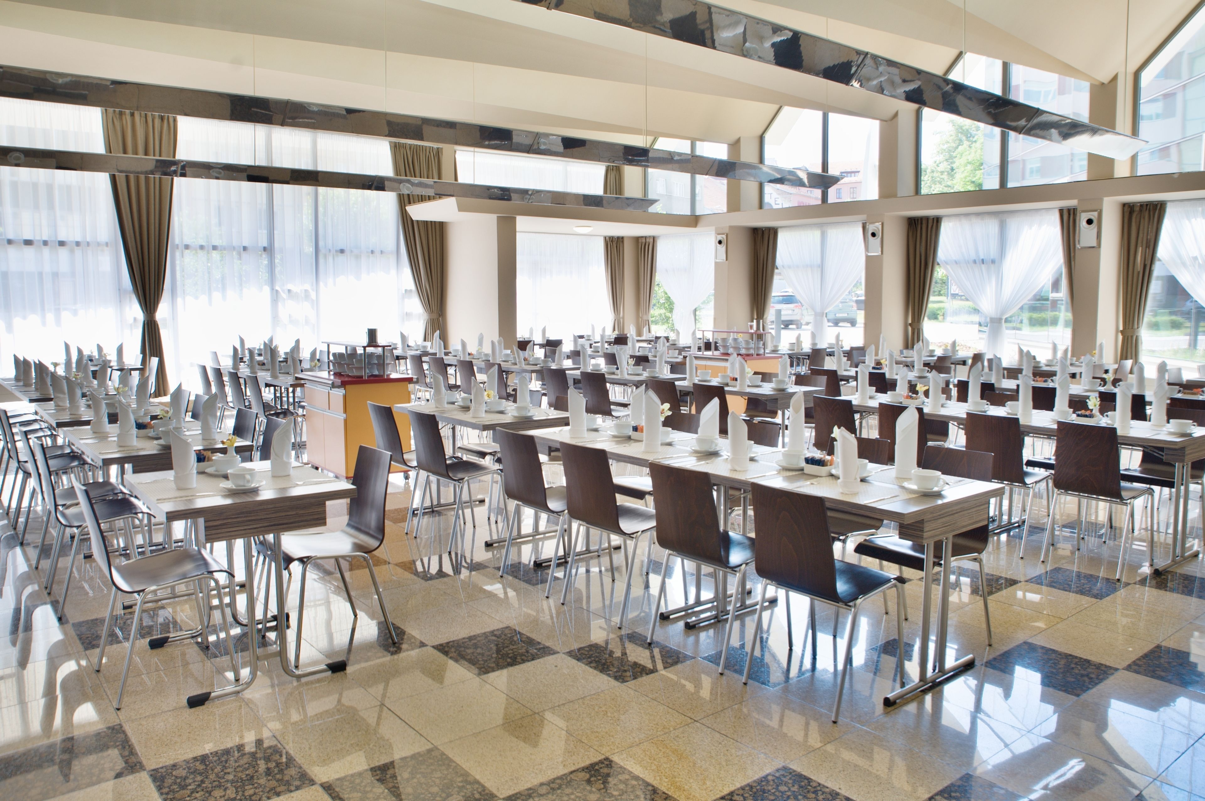 A spacious dining area with multiple tables and chairs, large windows, and a modern interior design.
