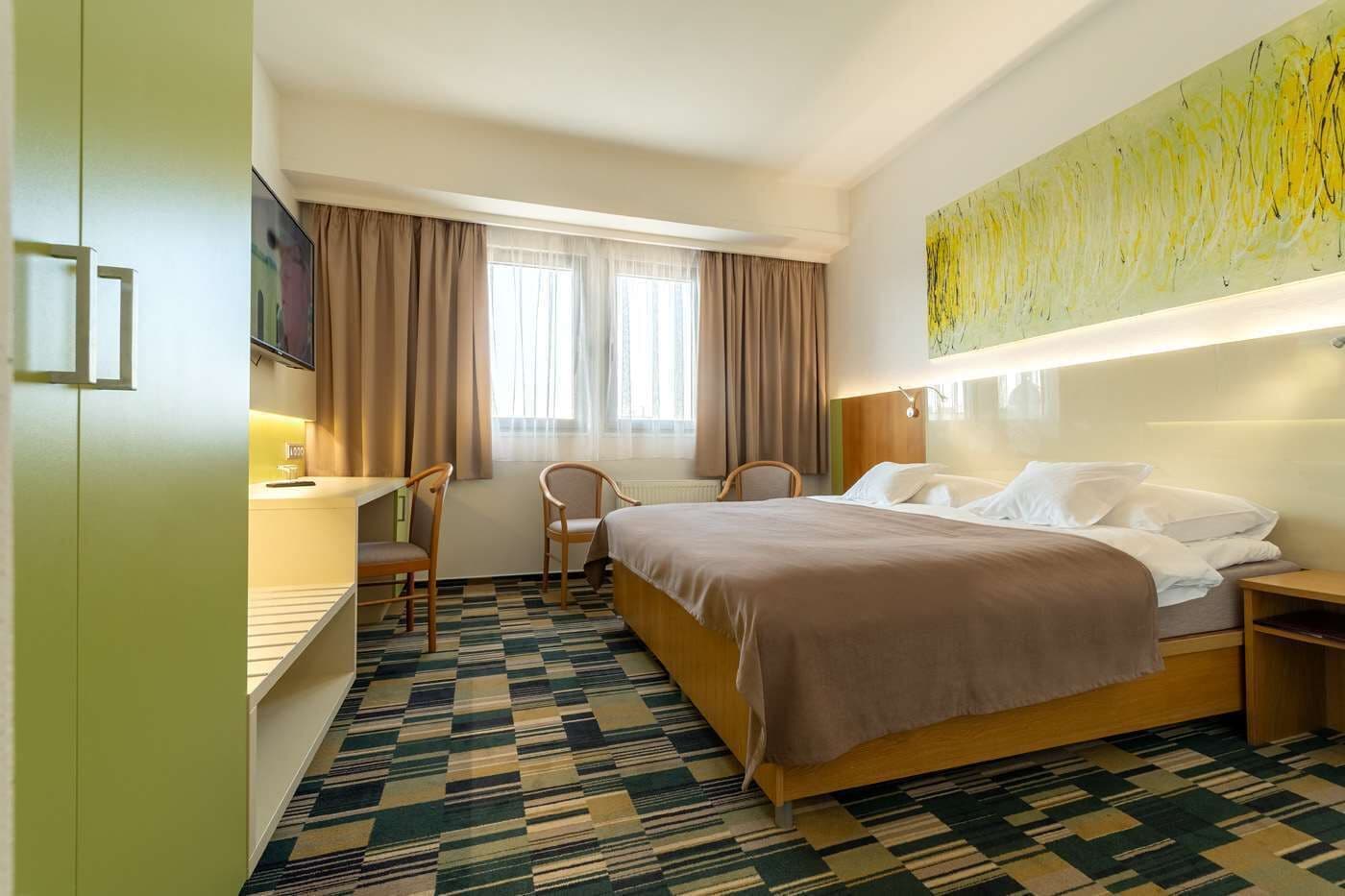 A hotel room with a bed, two chairs, a desk, and a TV.