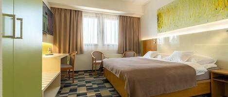 A hotel room with a bed, two chairs, a desk, and a TV.