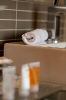 Un baño con una toalla sobre un banco, un vaso de líquido ámbar y una pared de azulejos.