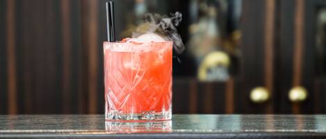 A cocktail with a straw and ice cubes in a glass with a textured pattern, placed on a dark wooden surface.