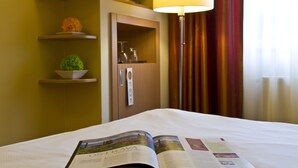 A hotel room with a bed, a magazine, a television on a shelf, a lamp, and a door with a handle. - Imperial Hotel Ostrava (Ostrava)