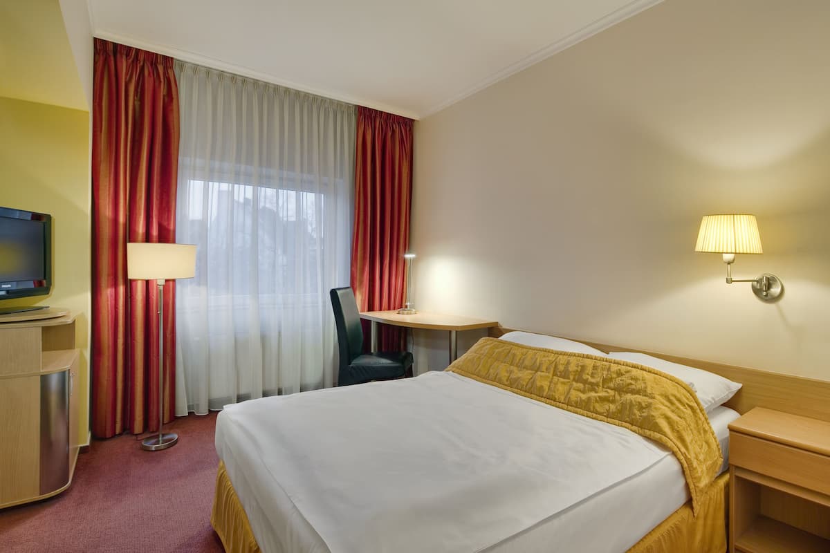 Habitación de hotel con cama, escritorio con televisor, una silla, lámpara y mesita de noche.