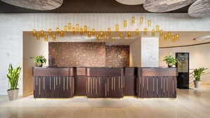A modern reception desk with a patterned wall, pendant lighting, and potted plants. - Imperial Hotel Ostrava (Ostrava)