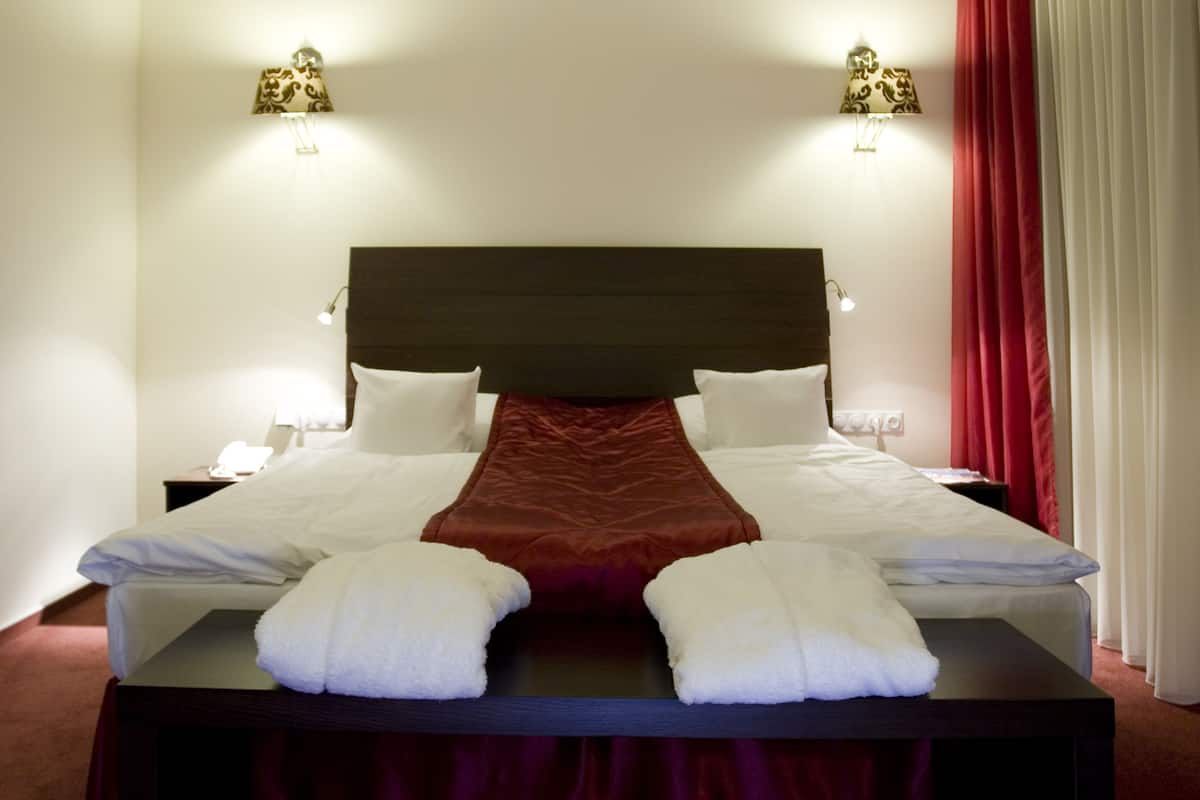 Una cama bien hecha con sábanas blancas, una almohada decorativa roja y dos lámparas de noche.