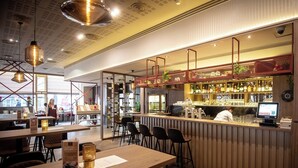 A modern bar area with a wooden counter, bar stools, and a digital menu display. - Imperial Hotel Ostrava (Ostrava)