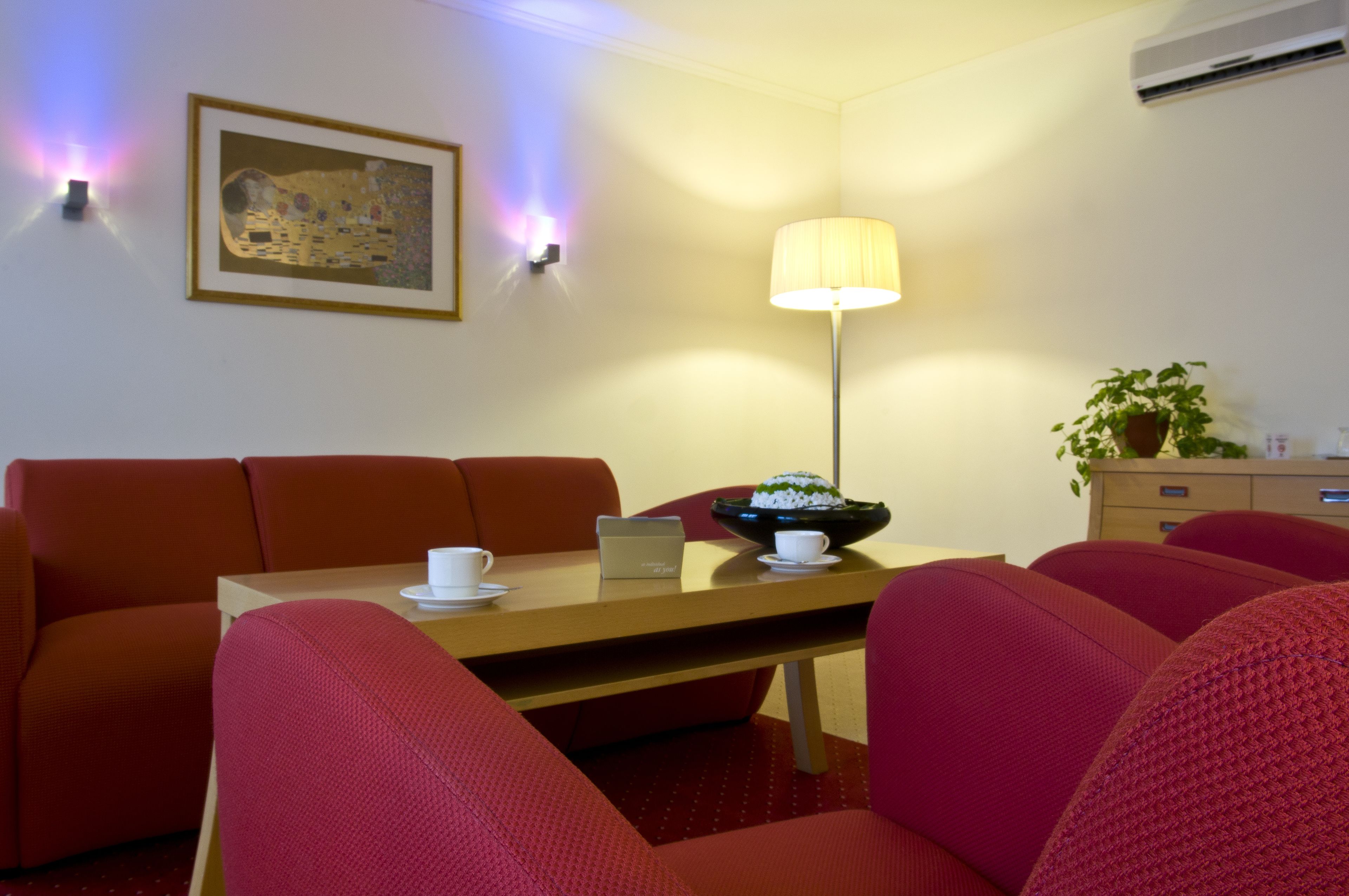 A dining area with a table, chairs, a lamp, a painting, and a potted plant.