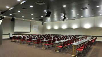 A conference room with rows of tables and chairs, a projector screen, and a podium.