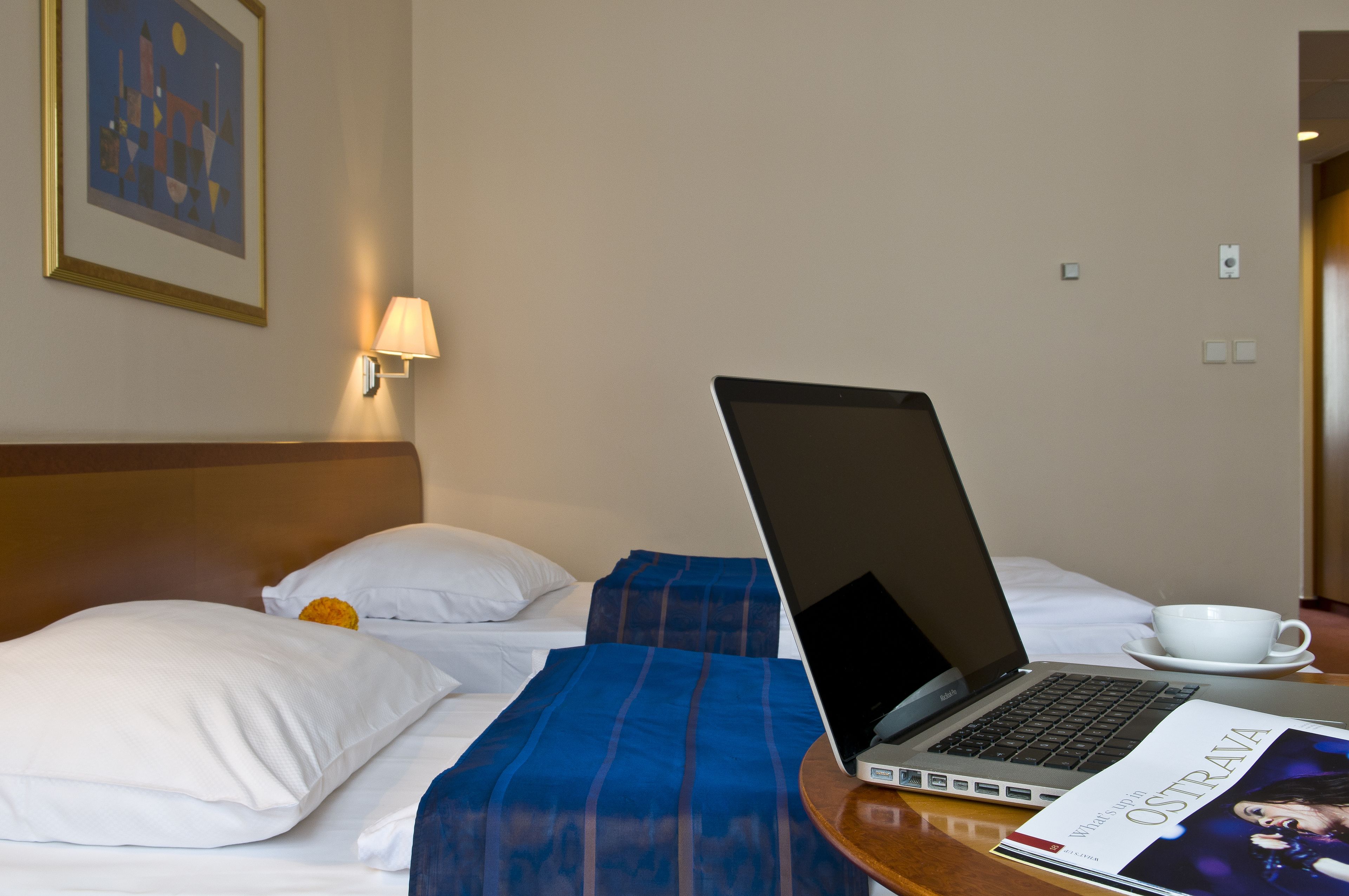 Quarto de hotel com uma cama, um laptop, uma xícara e uma revista sobre a mesa.