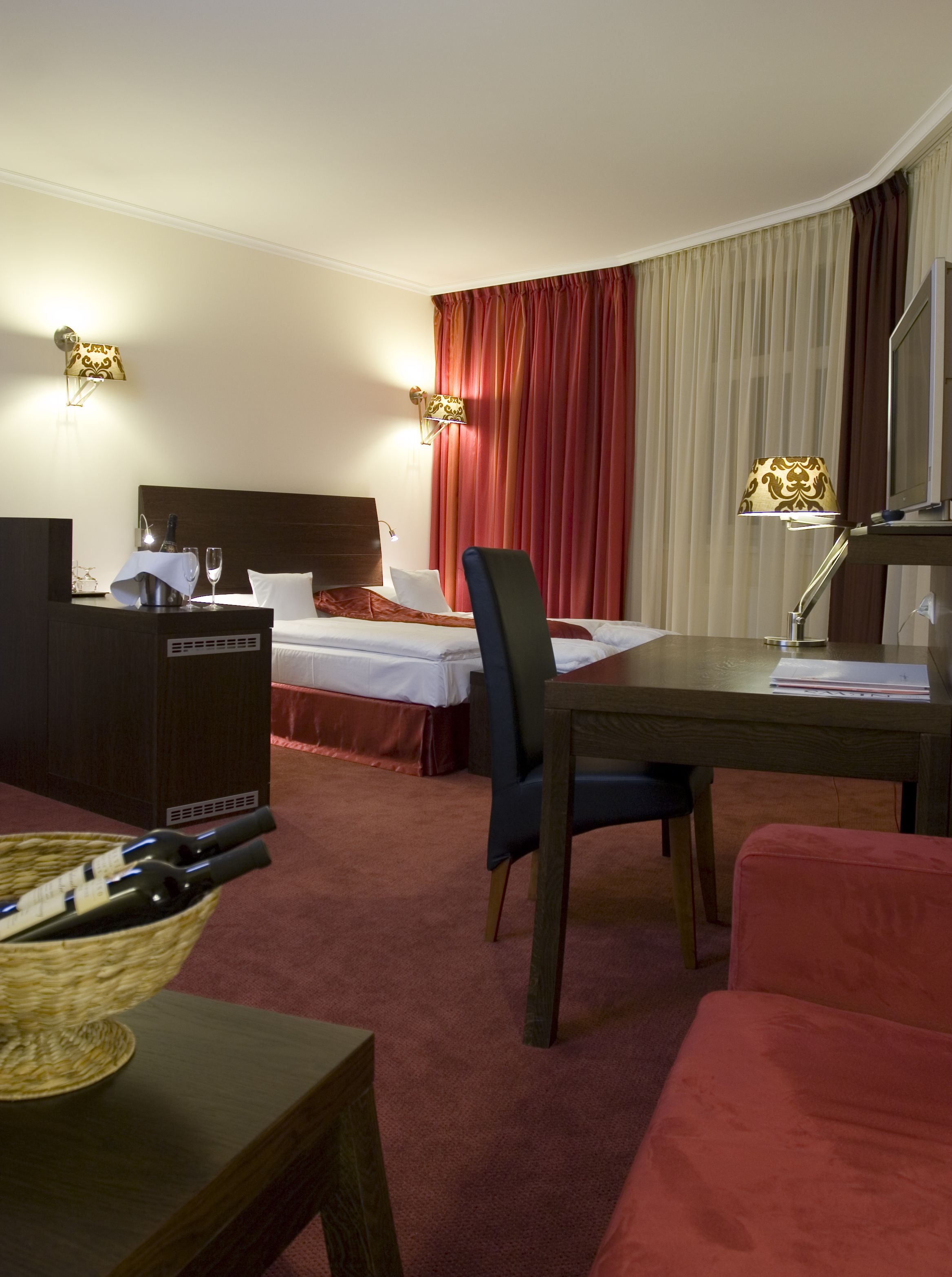 A hotel room with a bed, a desk, a chair, a TV, and a minibar.