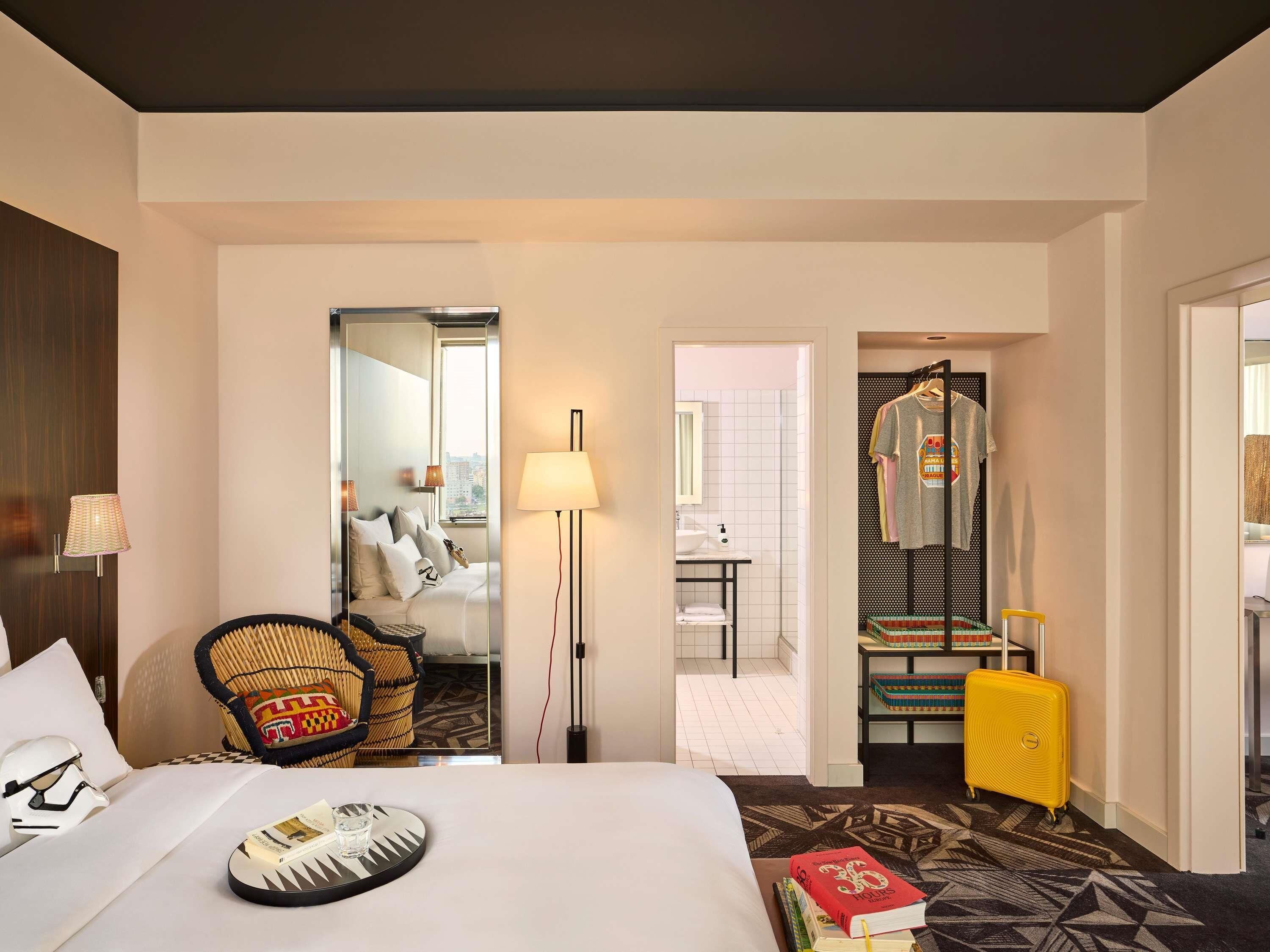 Ein Hotelzimmer mit Bett, Sessel, Lampe, Koffer und angrenzendem Badezimmer.