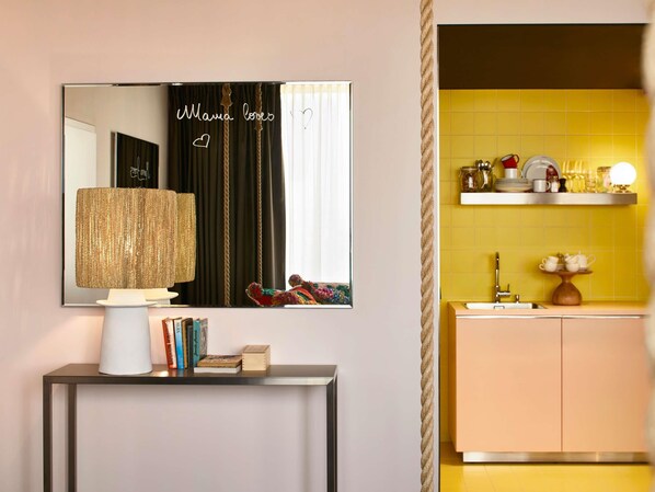 A modern interior with a mirror reflecting a room, a lamp on a console table, and a kitchen area with yellow tiles and a sink.