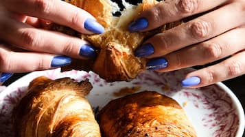 Ein Nahblick auf Hände, die einen Croissant halten, ein weiteres Croissant ist auf einem Teller teilweise sichtbar.