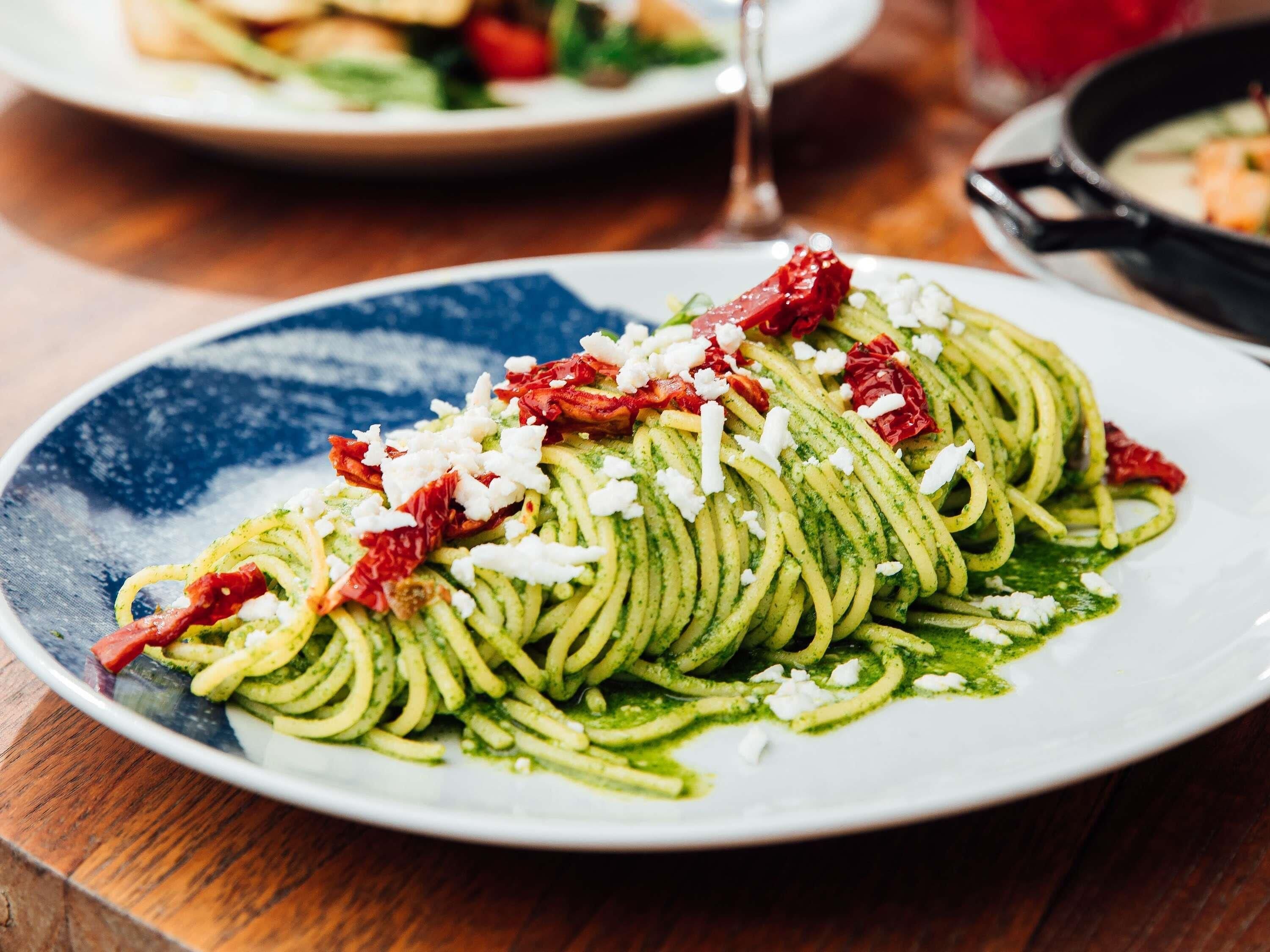 Een bord pasta met pesto, zongedroogde tomaten en kaas.