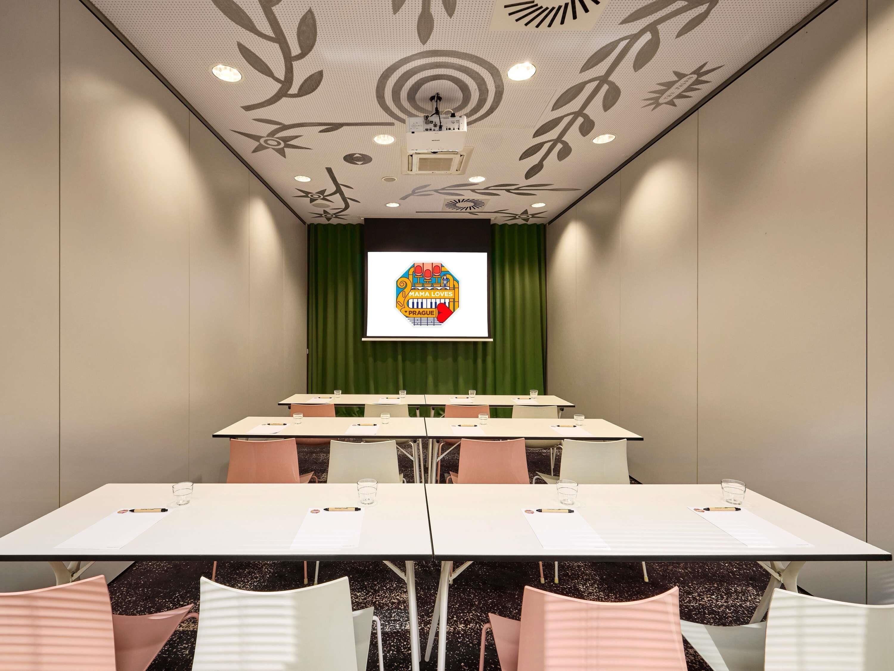 Un salón de conferencias con un telón de fondo verde, una pantalla de proyector y un techo con estampado floral.