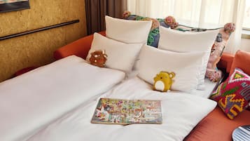 Uma cama com roupa de cama branca, um cobertor colorido e um bicho de pelúcia.