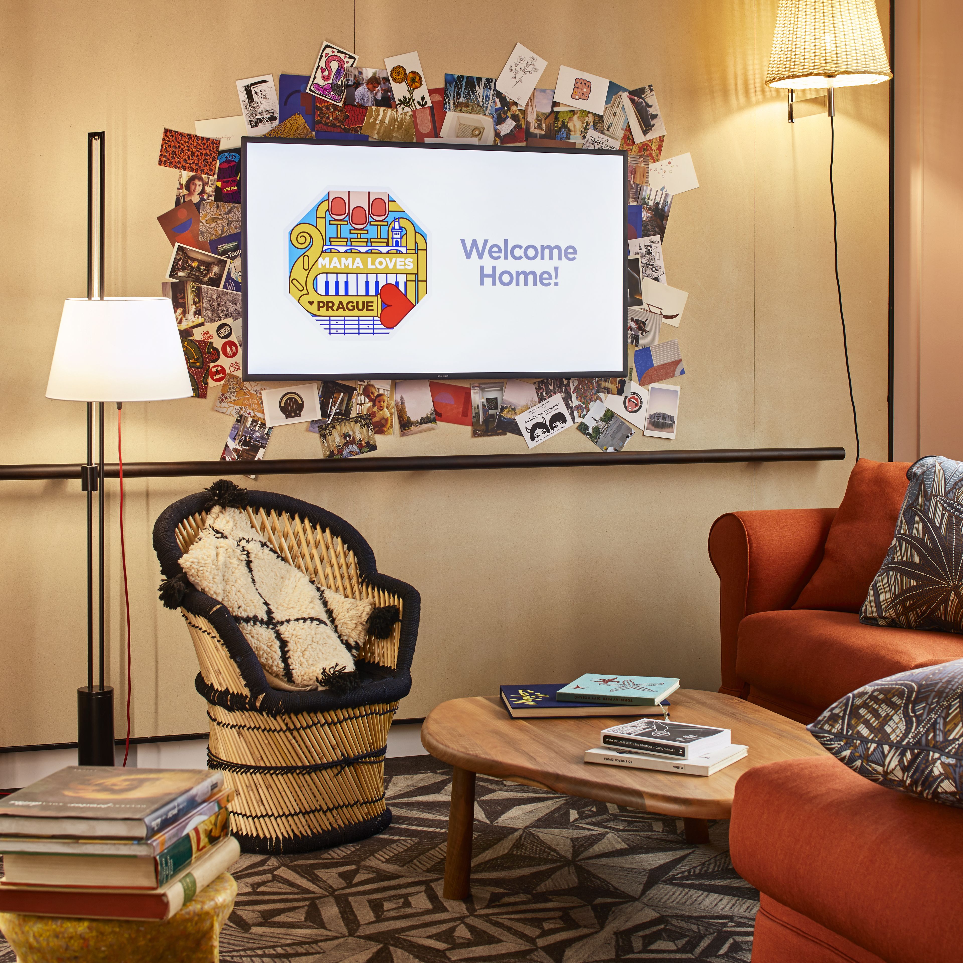 Een knus ingerichte kamer met een televisie waarop een welkomstboodschap staat, een rieten stoel, een bijzettafeltje met boeken en een kamerkleed met een patroon.
