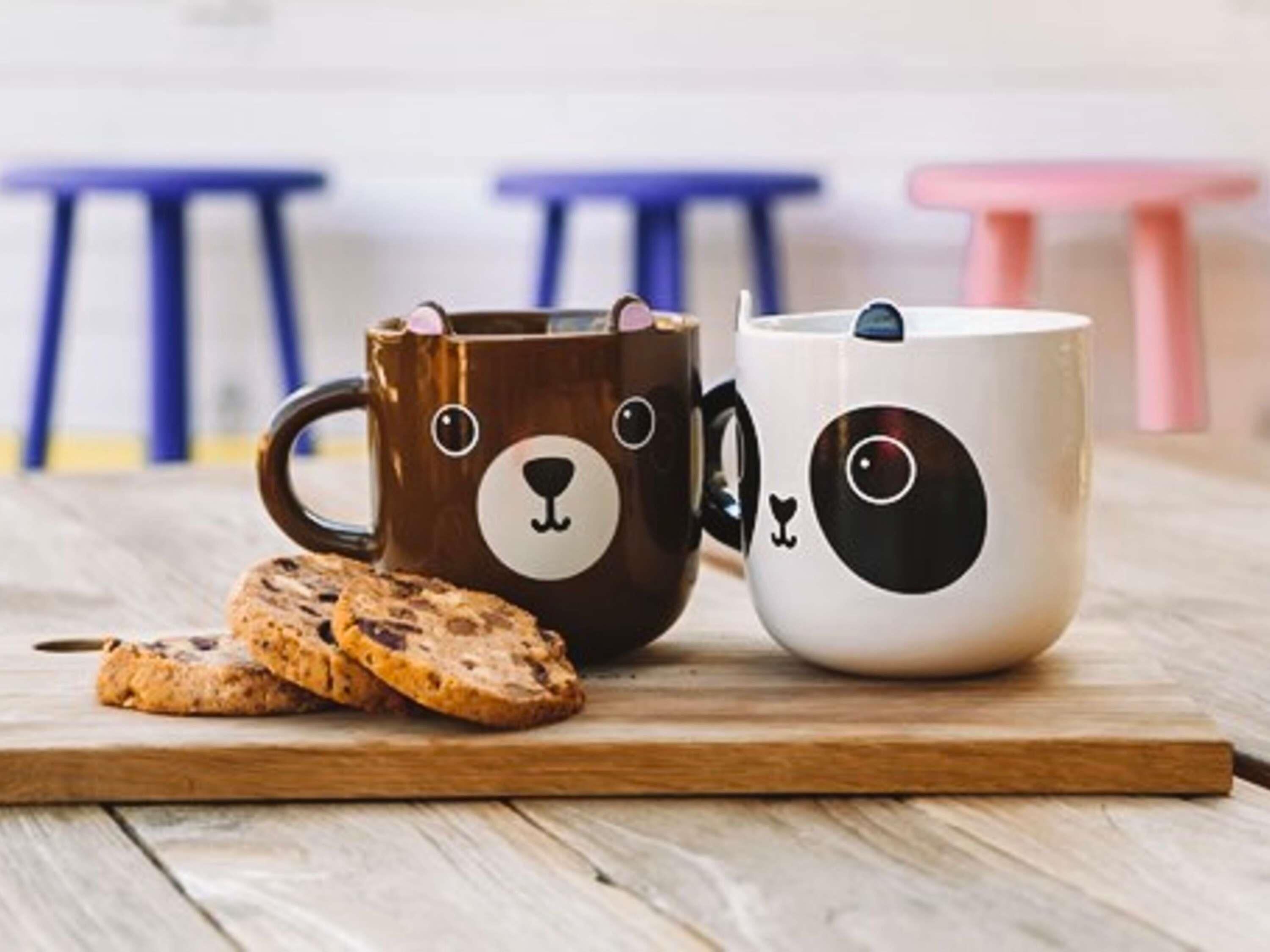 Two mugs with bear faces, a wooden cutting board, and cookies.