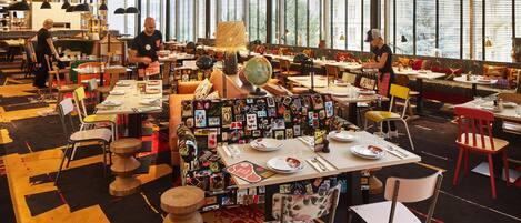 A restaurant with multiple tables and chairs, large windows, and a variety of table settings.