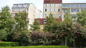 A row of multi-story buildings with balconies, surrounded by well-maintained hedges and flowering trees.