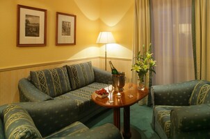 Een gezellige kamer met een groene sofa met patroon, een klein houten tafeltje met een bloevas, en twee ingelijste foto's aan de muur.