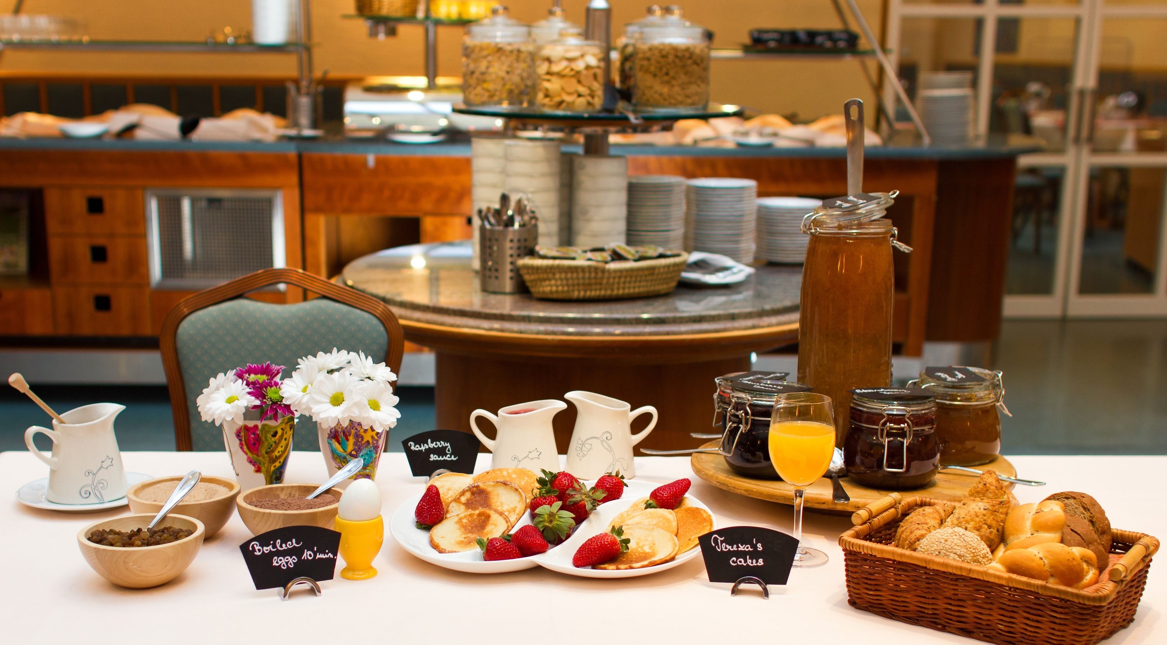 A breakfast buffet with various food items, including pancakes, strawberries, and bread. There are also several pitchers and jars of condiments.