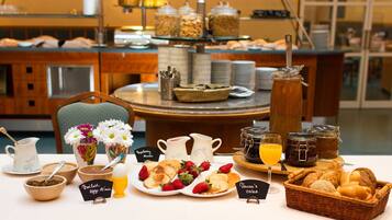 A breakfast buffet with various food items, including pancakes, strawberries, and bread. There are also several pitchers and jars of condiments.