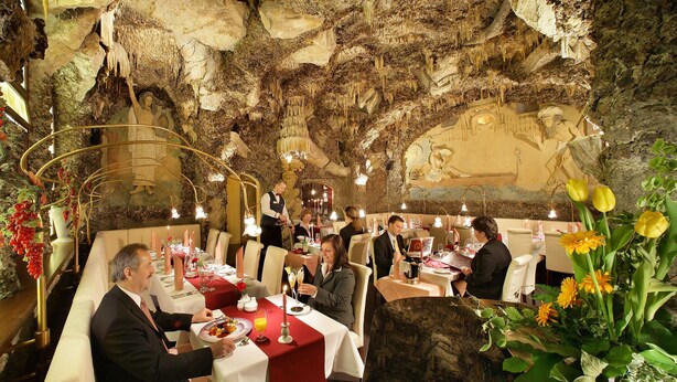 A restaurant with a cave-like interior, tables set with red tablecloths, and diners. - Adria Hotel Prague (Prague)