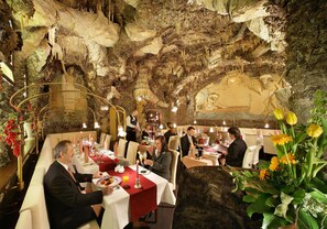 A restaurant with a cave-like interior, tables set with red tablecloths, and diners. - Adria Hotel Prague (Prague)