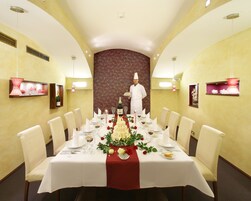 Una sala da pranzo formale con un lungo tavolo apparecchiato per un pasto, un cameriere sullo sfondo e decorazioni murali.