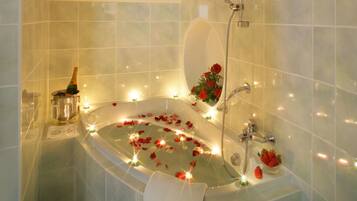 A bathtub with rose petals, champagne, and strawberries.