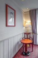 Quarto nos cantos com um quadro enquadrado na parede, um abajur, uma cadeira de madeira e um tapete estampado.