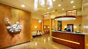 A hotel lobby with a reception desk, a statue, a staircase, and a seating area. - Adria Hotel Prague (Prague)
