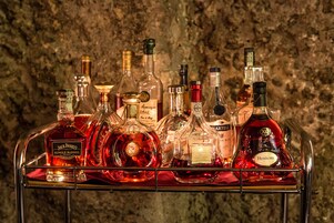 Coleção de garrafas de licor sobre um carrinho de metal, em frente a uma parede texturizada.