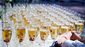 Una fila di bicchieri da champagne riempiti con una bevanda dorata e guarniti con bacche rosse, su un tavolo.