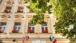 A building with a sign reading "HOTEL ADRIA" and multiple windows with red flowers. Flags are displayed in front of the entrance. - Adria Hotel Prague (Prague)