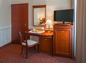 Quarto de hotel com uma escrivaninha de madeira, televisão em um móvel, uma cadeira e um espelho.