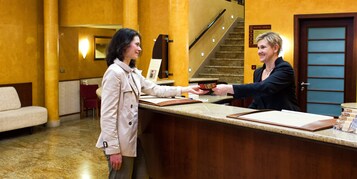 Uma área de recepção de hotel com balcão, escada e placa indicando o endereço do hotel.