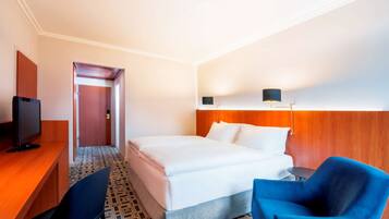 A hotel room with a bed, a desk with a TV, a chair, and a lamp.
