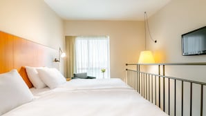 A hotel room with a large bed, a desk, a chair, a TV mounted on the wall, and a window with curtains. - NH Prague City (Prague)