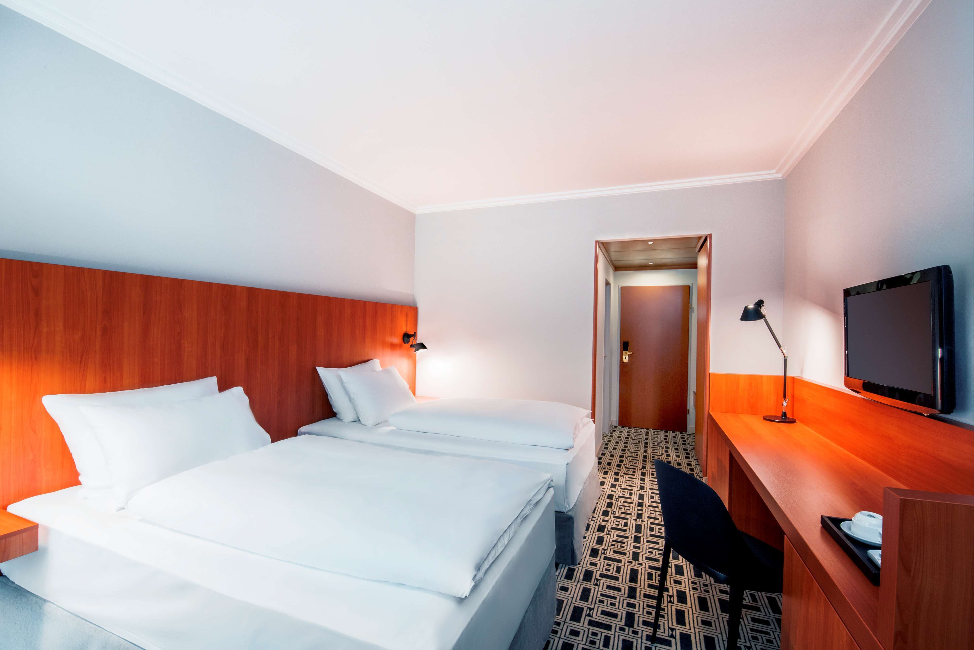 A hotel room with a large bed, a desk with a TV, and a door leading to another room.