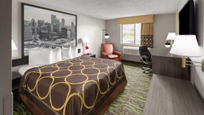 Una habitación de hotel con una cama grande, un escritorio, una silla, una lámpara de escritorio y un cuadro de una vista urbana en la pared.