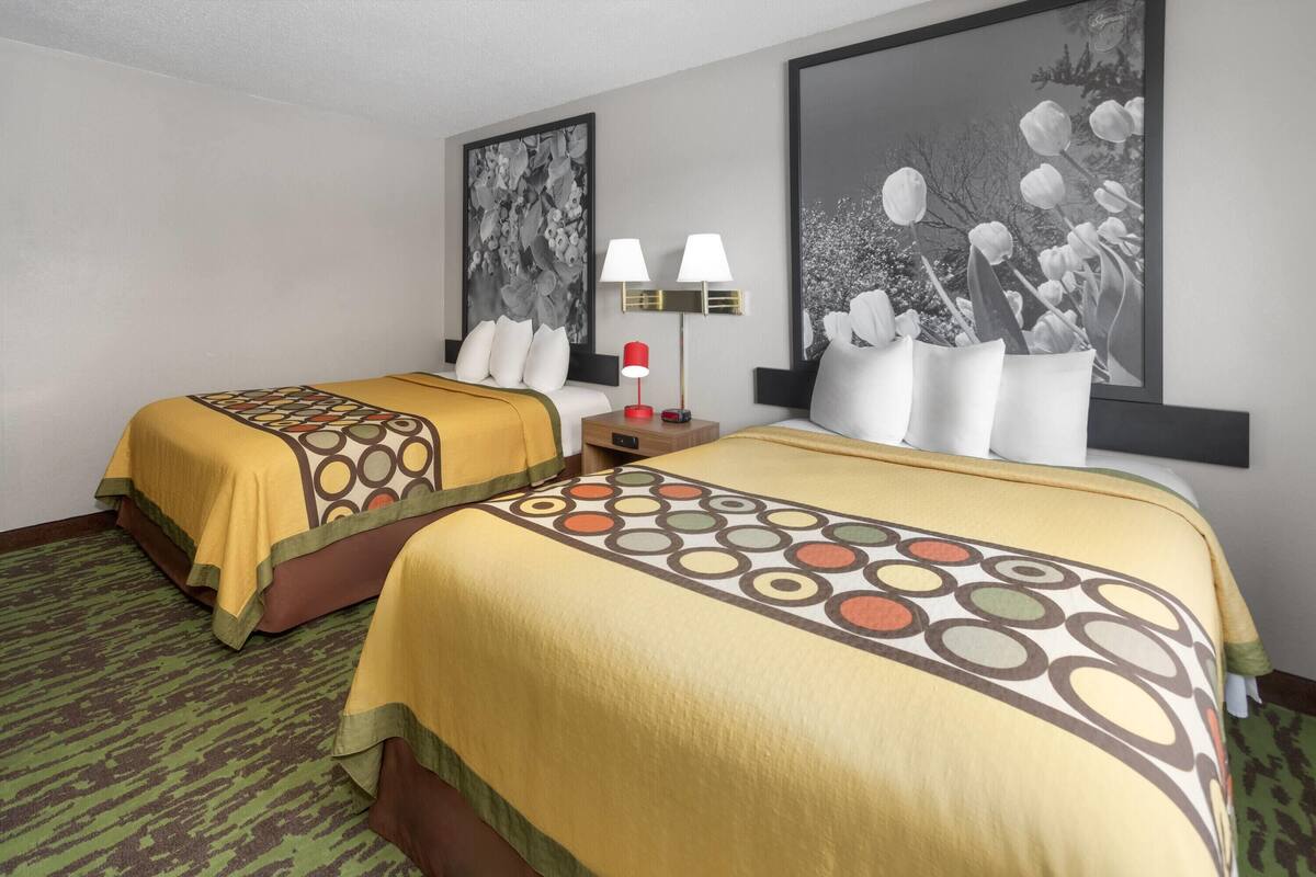 A hotel room with two beds, each with a patterned bedspread, a nightstand with a lamp, and two wall-mounted lamps.
