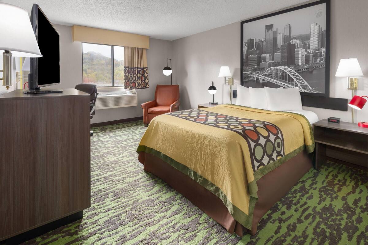 A hotel room with a bed, a desk, a chair, a TV, and a large window.